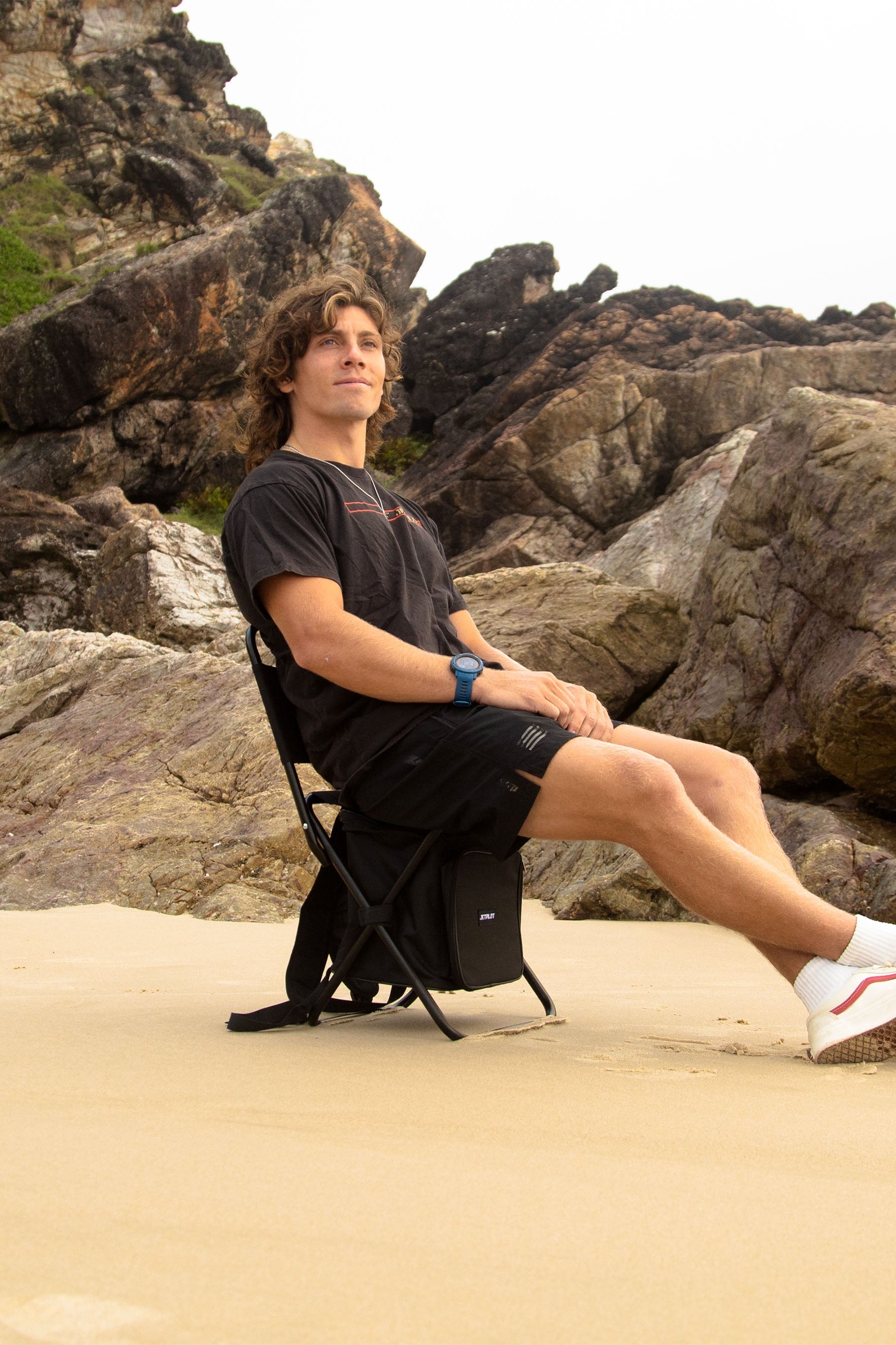 Person sitting on a folding Jetpilot Back Rest Chilled Seat Bag - Black on a rocky beach