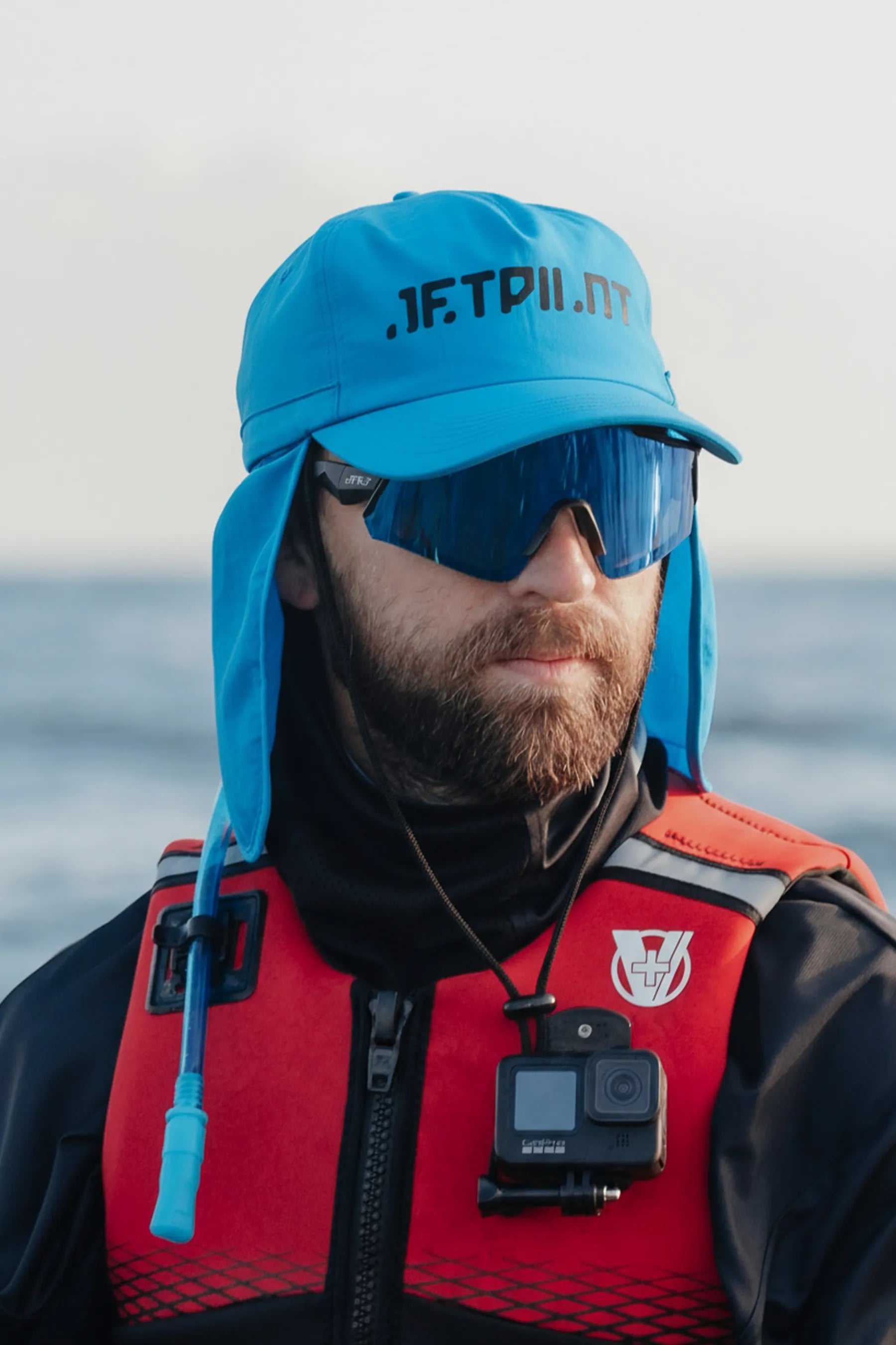 Person wearing a blue cap with 'JETPILOT' branding, sunglasses, and a red life jacket with a GoPro camera on a body of water.