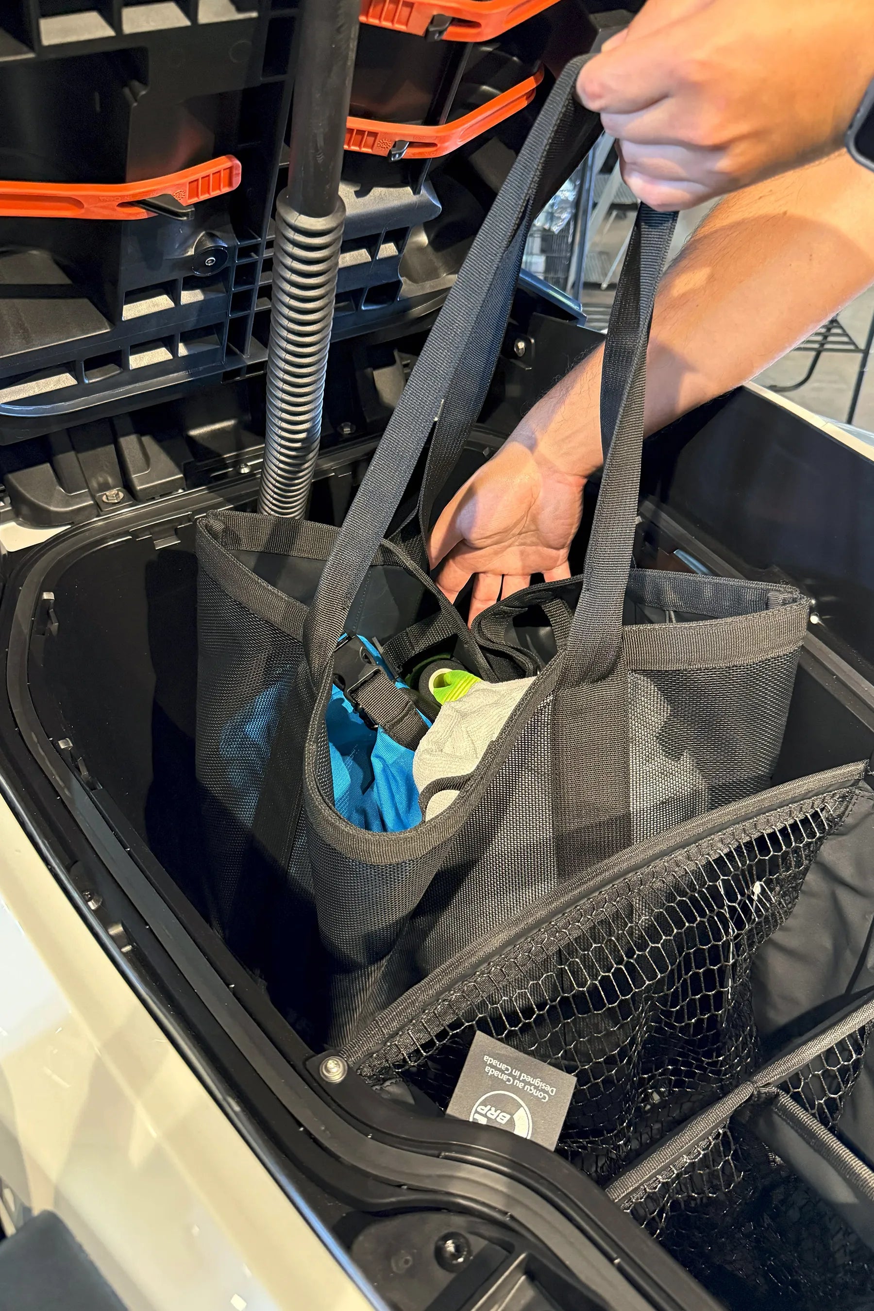 Person placing a black mesh bag into a jetski cargo area.