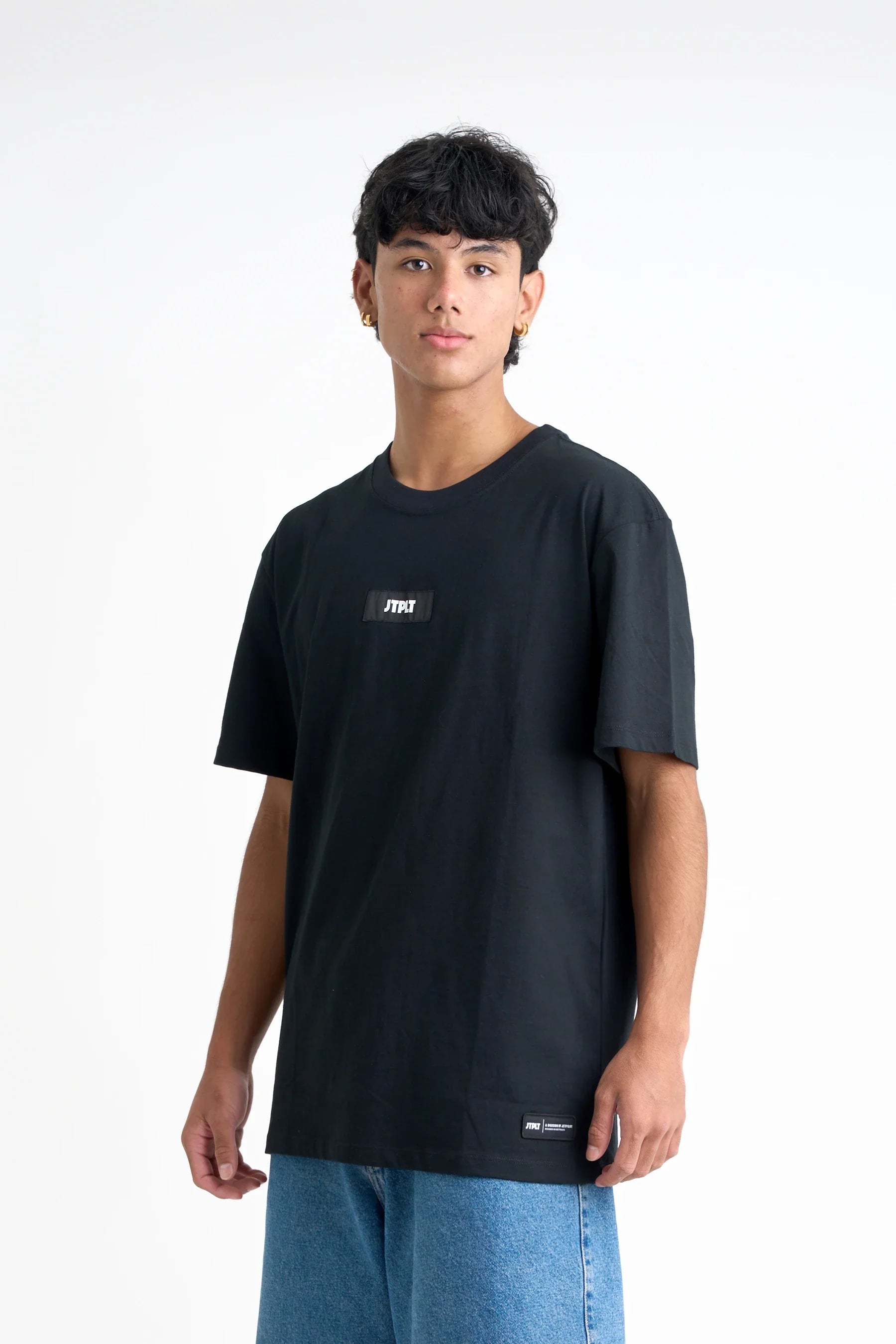 Person wearing a Jetpilot Staple Tee - Black t-shirt with a logo on a white background