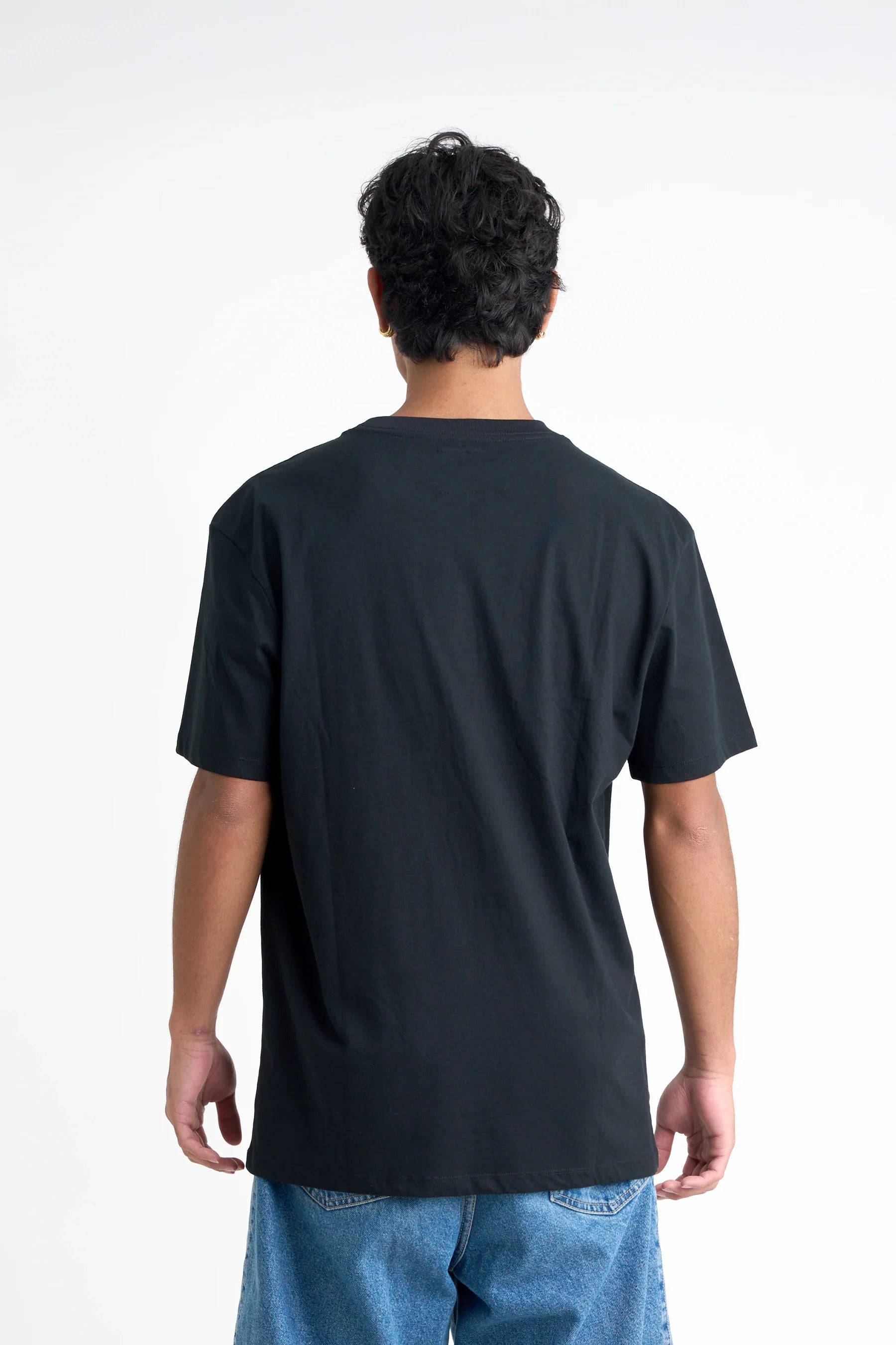 Back view of a man wearing a Jetpilot Staple Tee - Black t-shirt and blue jeans on a white background