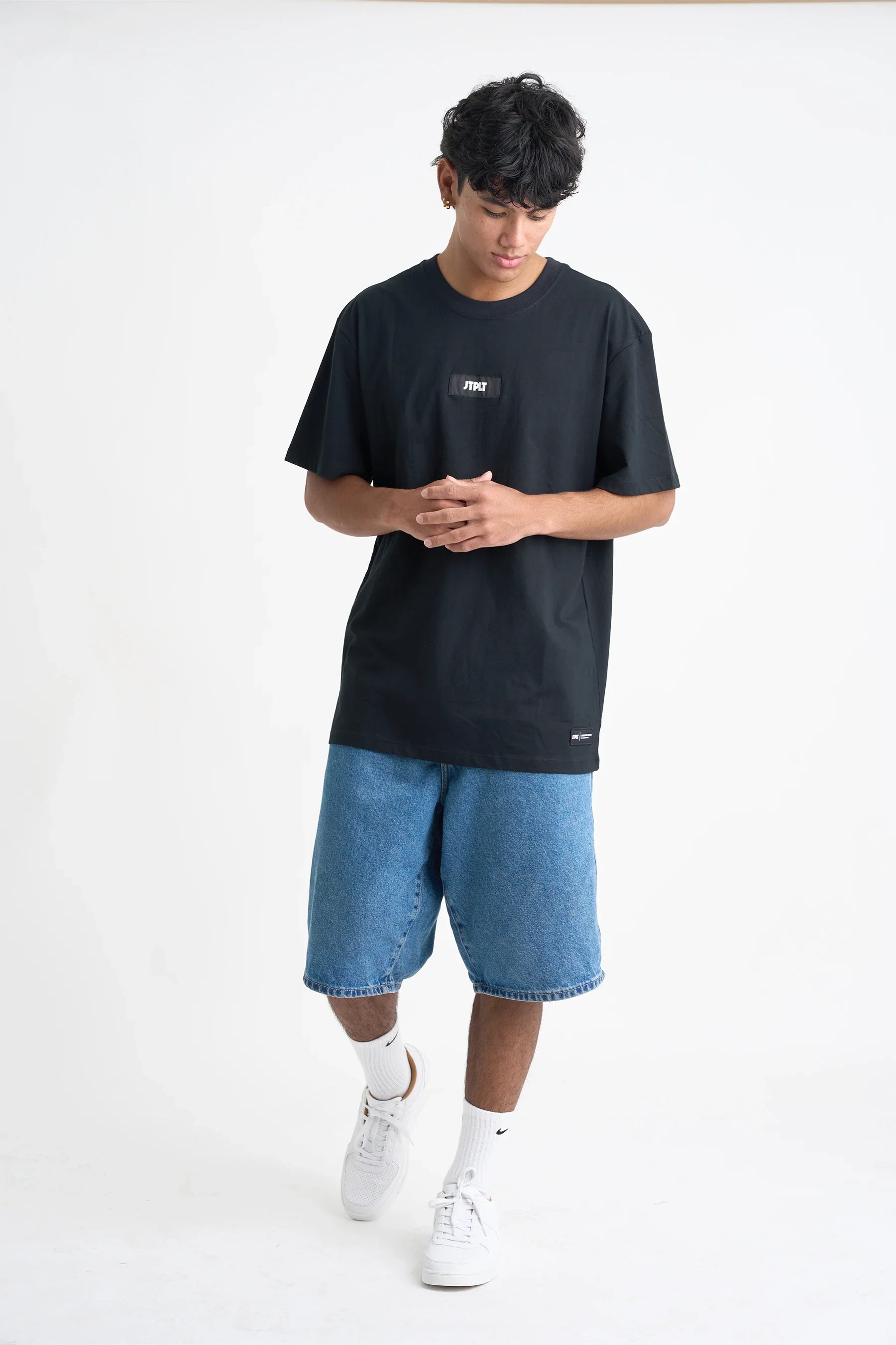 Person wearing a black t-shirt and blue shorts on a white background