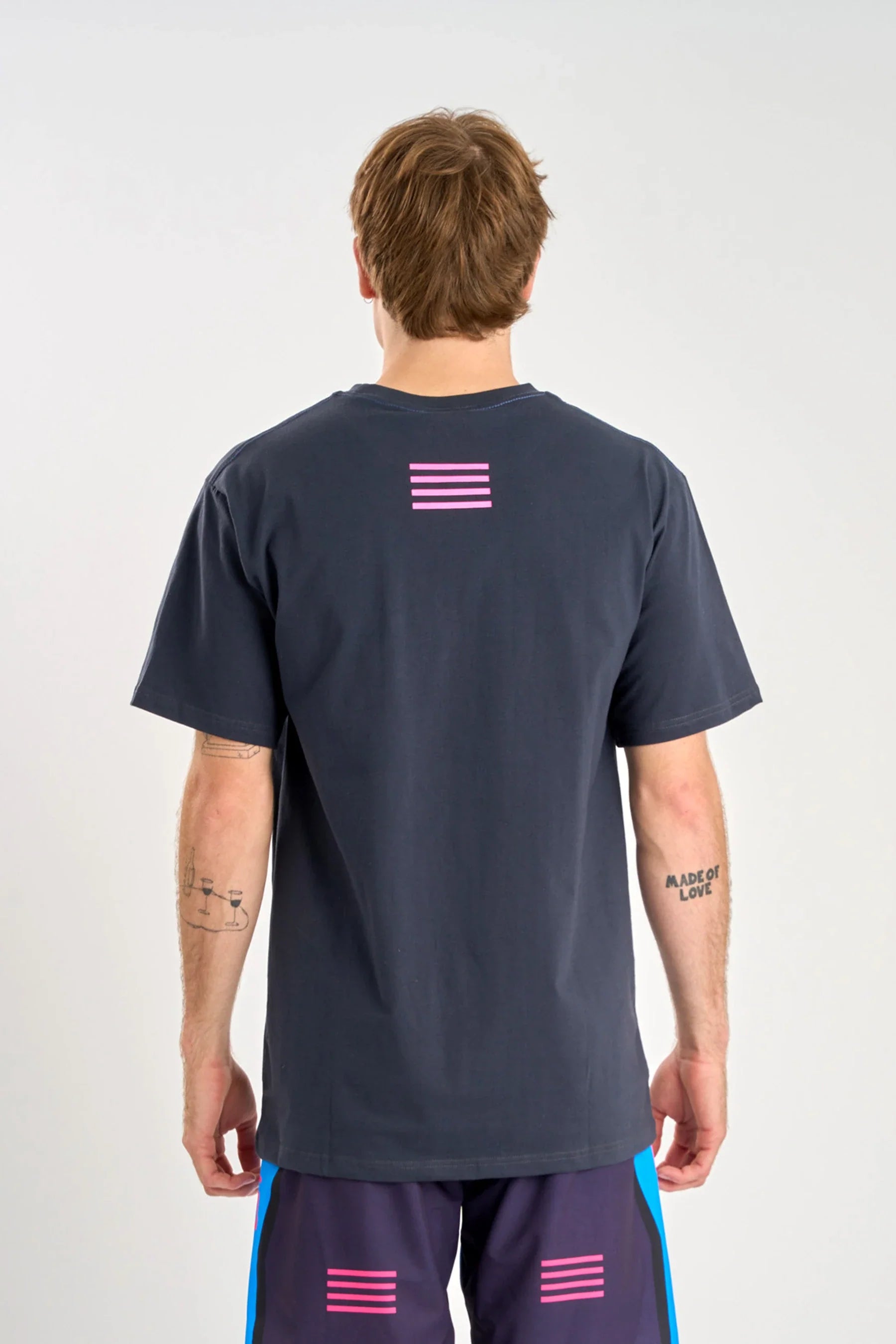 Person wearing a Jetpilot Vault SS Tee - Navy t-shirt with a pink flag design on the back, standing against a white background.
