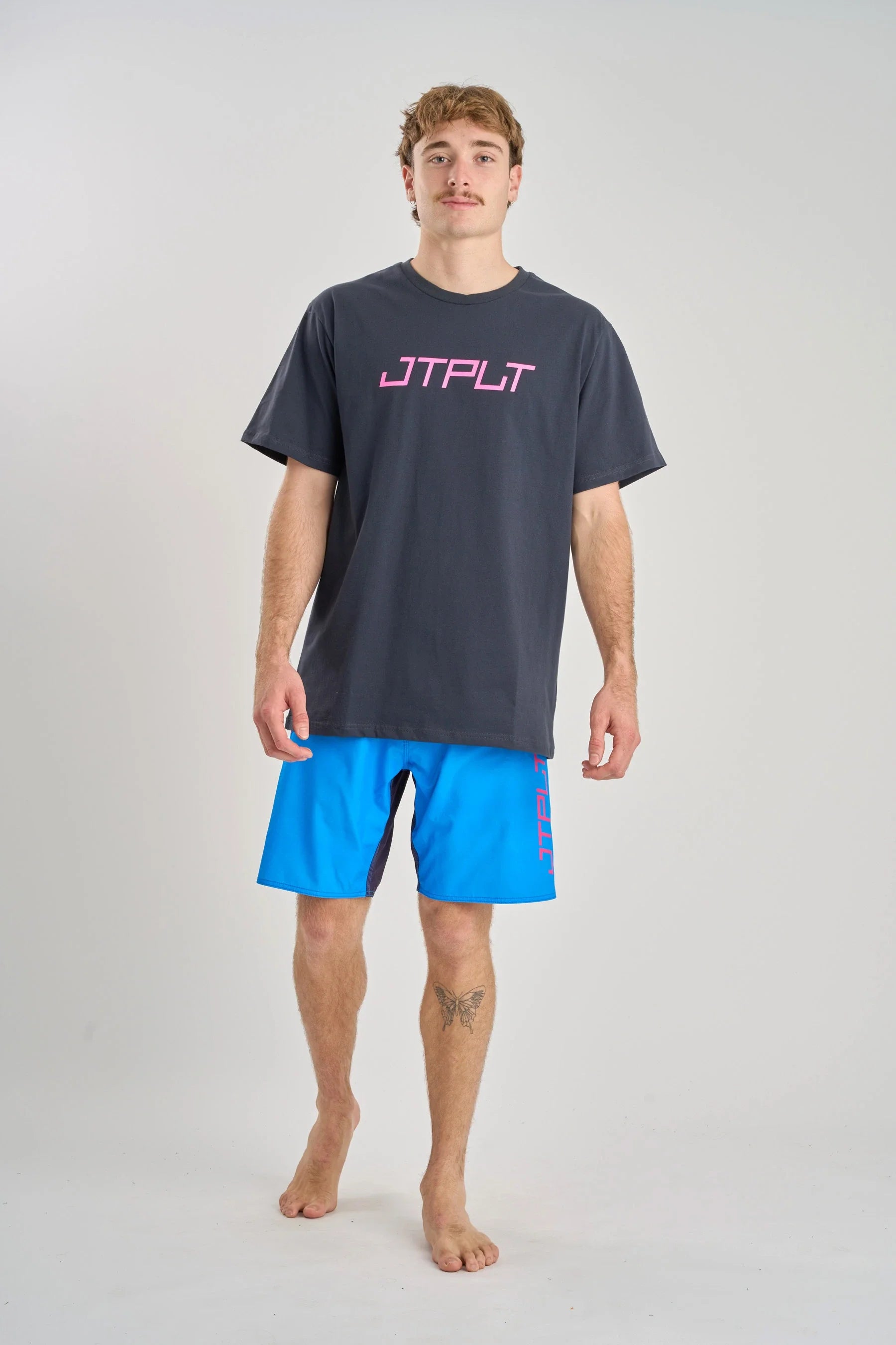 Man wearing a Jetpilot Vault SS Tee - Navy t-shirt with 'JTPLT' logo and blue shorts on a white background