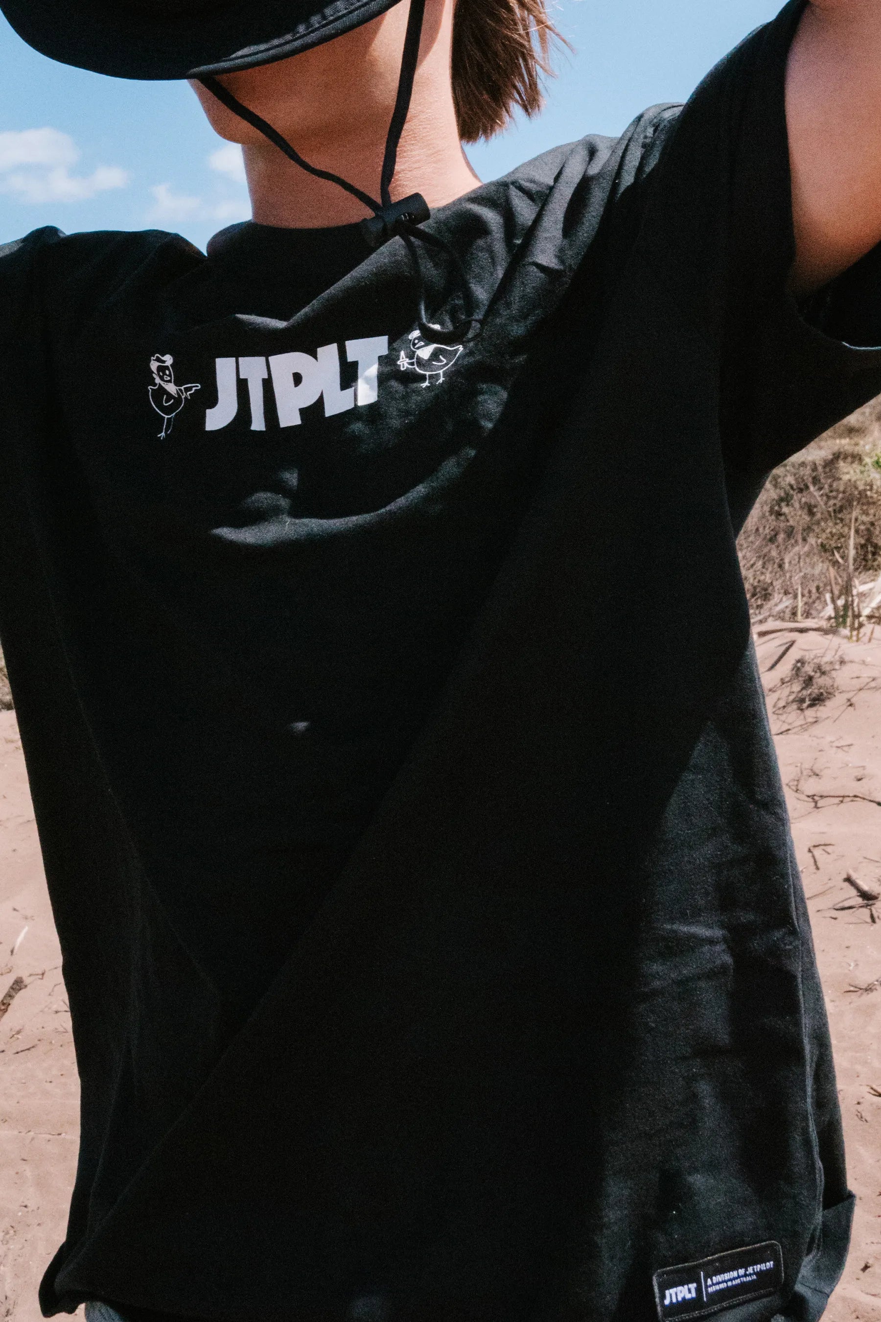 Person wearing a black t-shirt with 'JPTLT' branding outdoors.