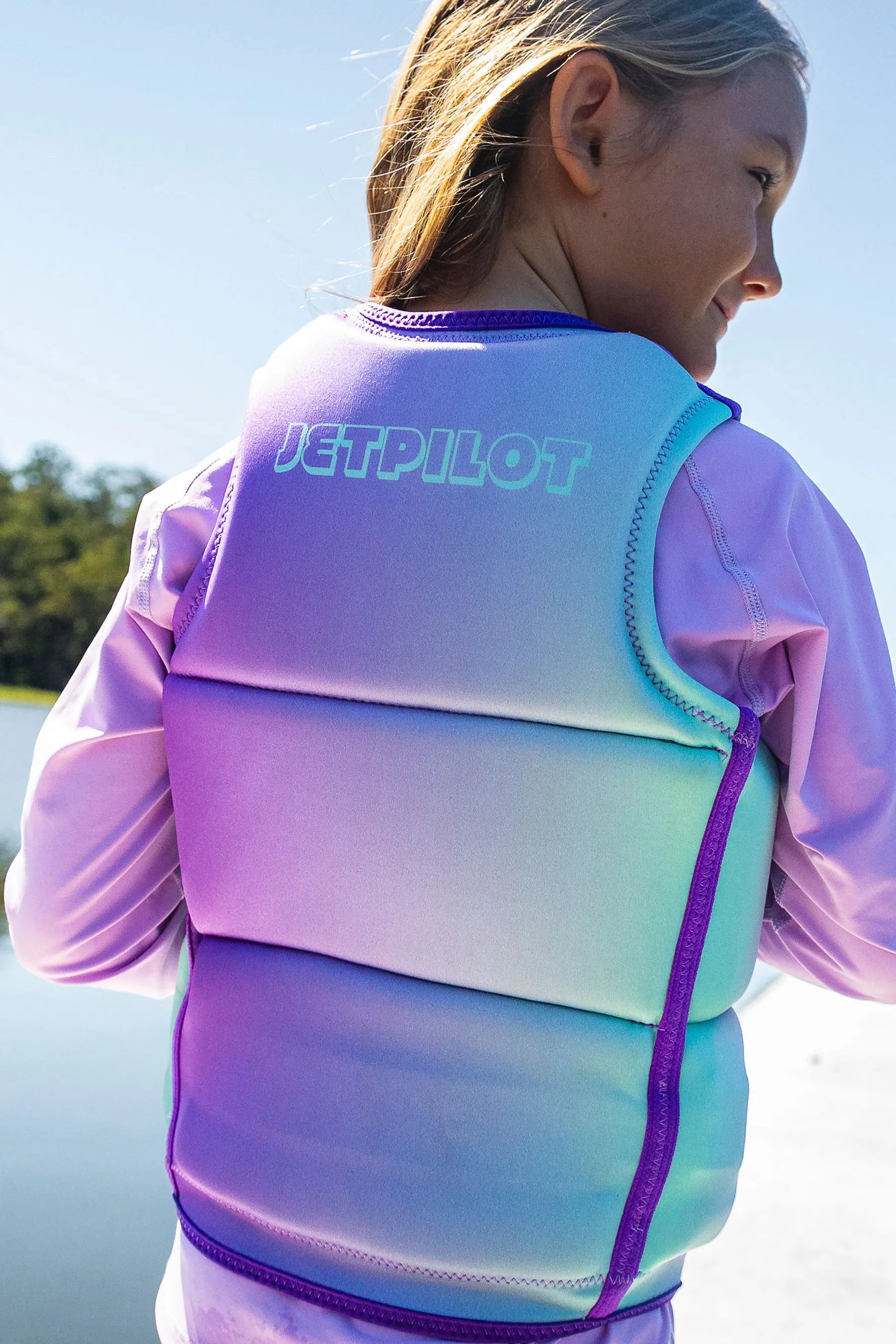 Girl wearing a Jetpilot Freeride Girls Life Jacket - Multi on a pontoon, with a body of water in the background