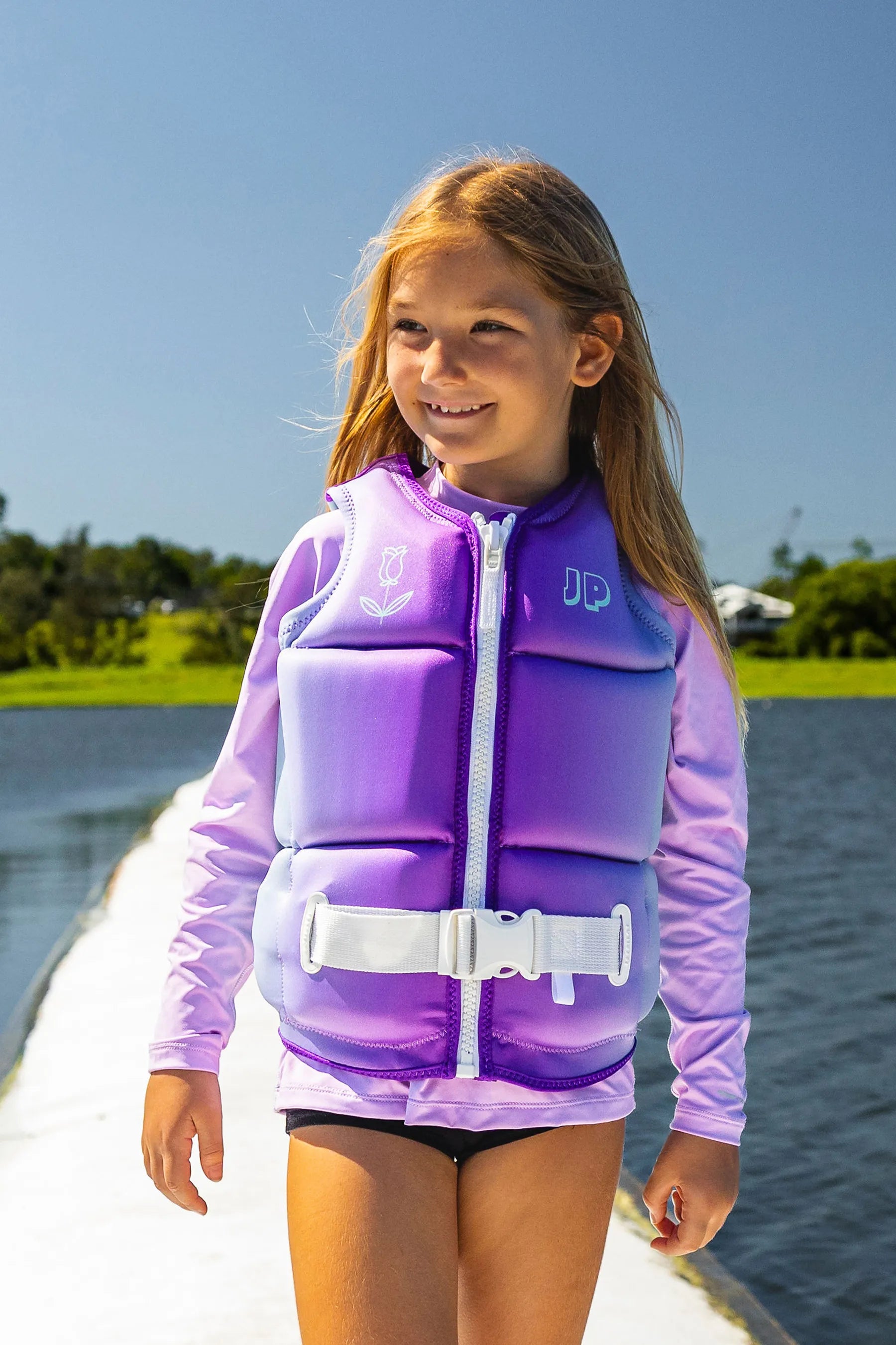 Girl in Jetpilot Freeride Girls Life Jacket - Multi on a pontoon, with a body of water in the background