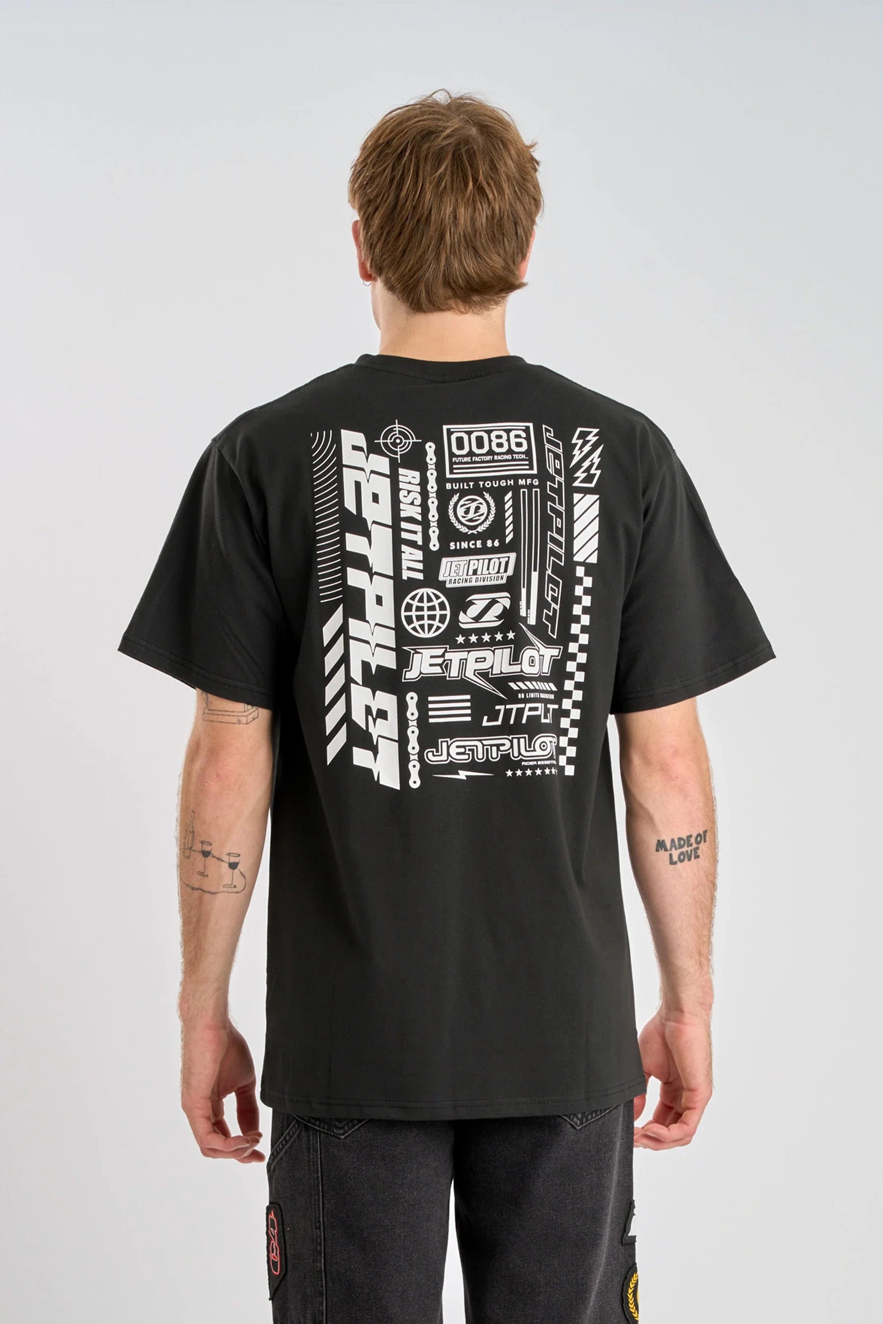 Person wearing a black Jetpilot Progressive t-shirt with white logo graphics and text on a plain background