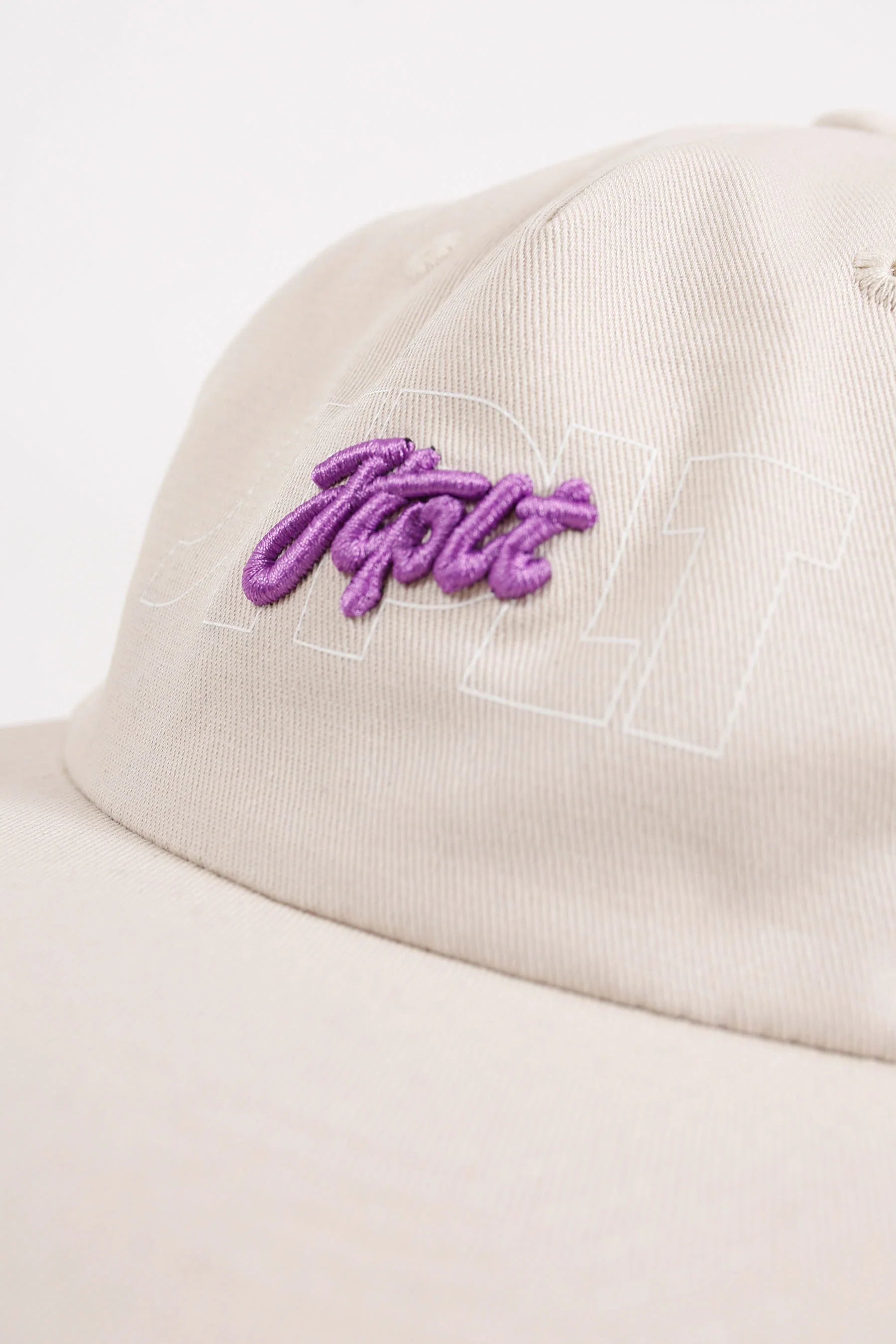 Beige cap with purple embroidered logo on a light gray background