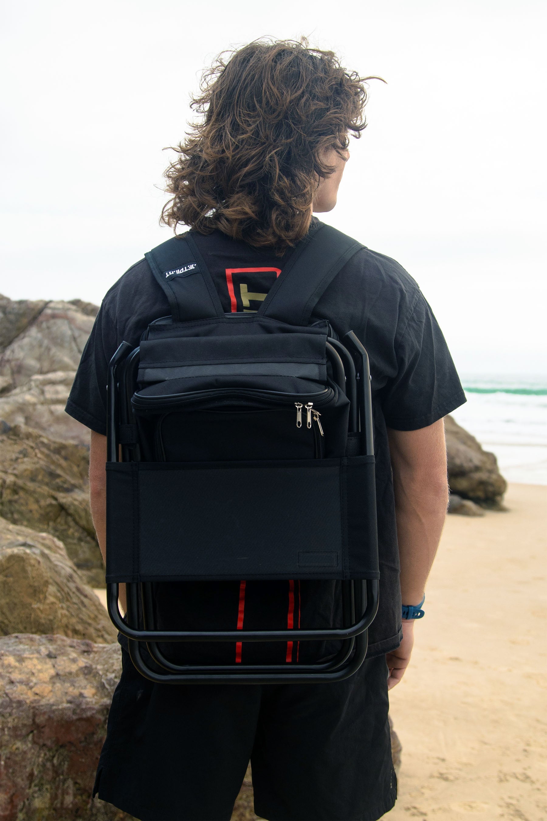 Person wearing a Jetpilot Back Rest Chilled Seat Bag - Black in backpack mode with a unique design on a beach