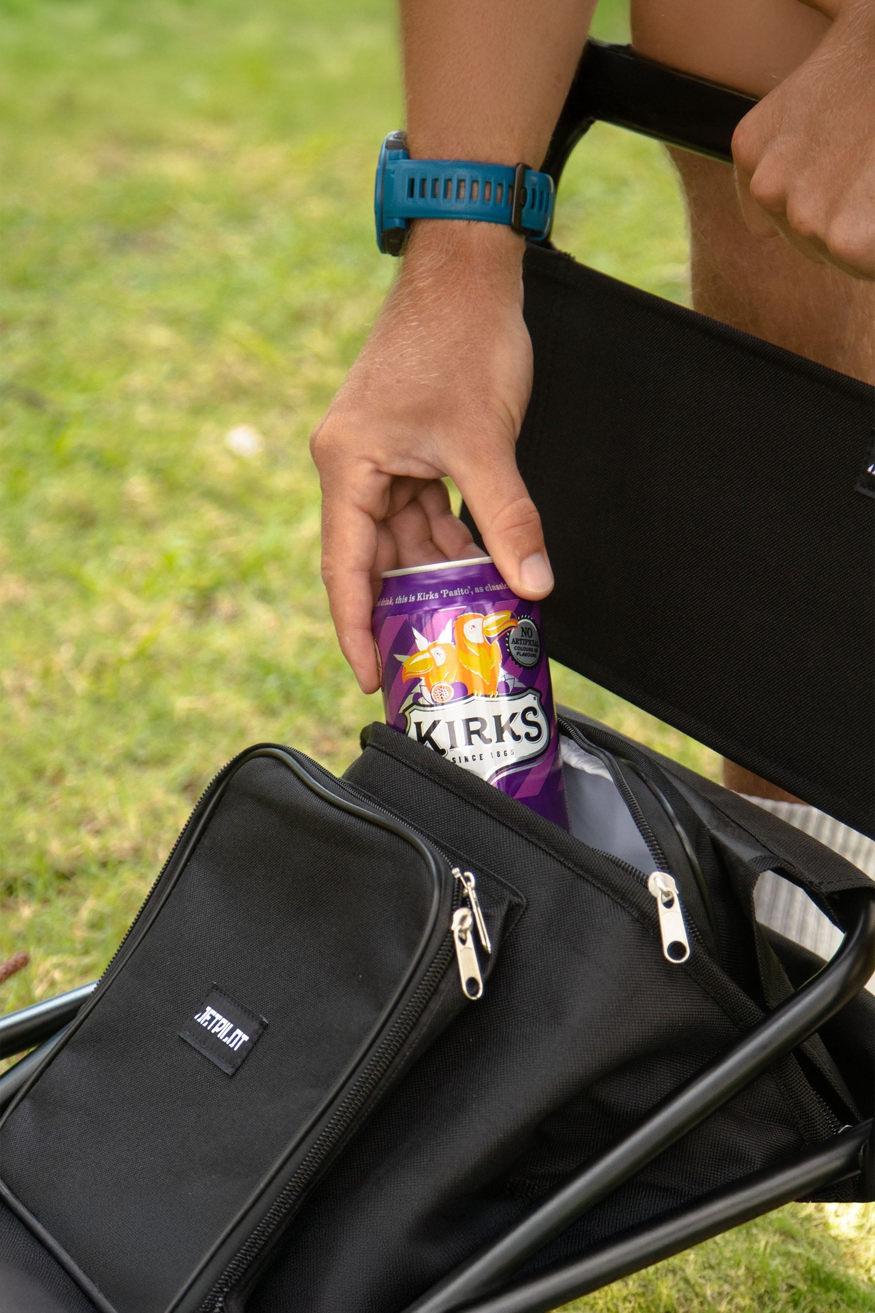 Person sitting outdoors with a Jetpilot Back Rest Chilled Seat Bag - Black and a purple can of Kirks Passito