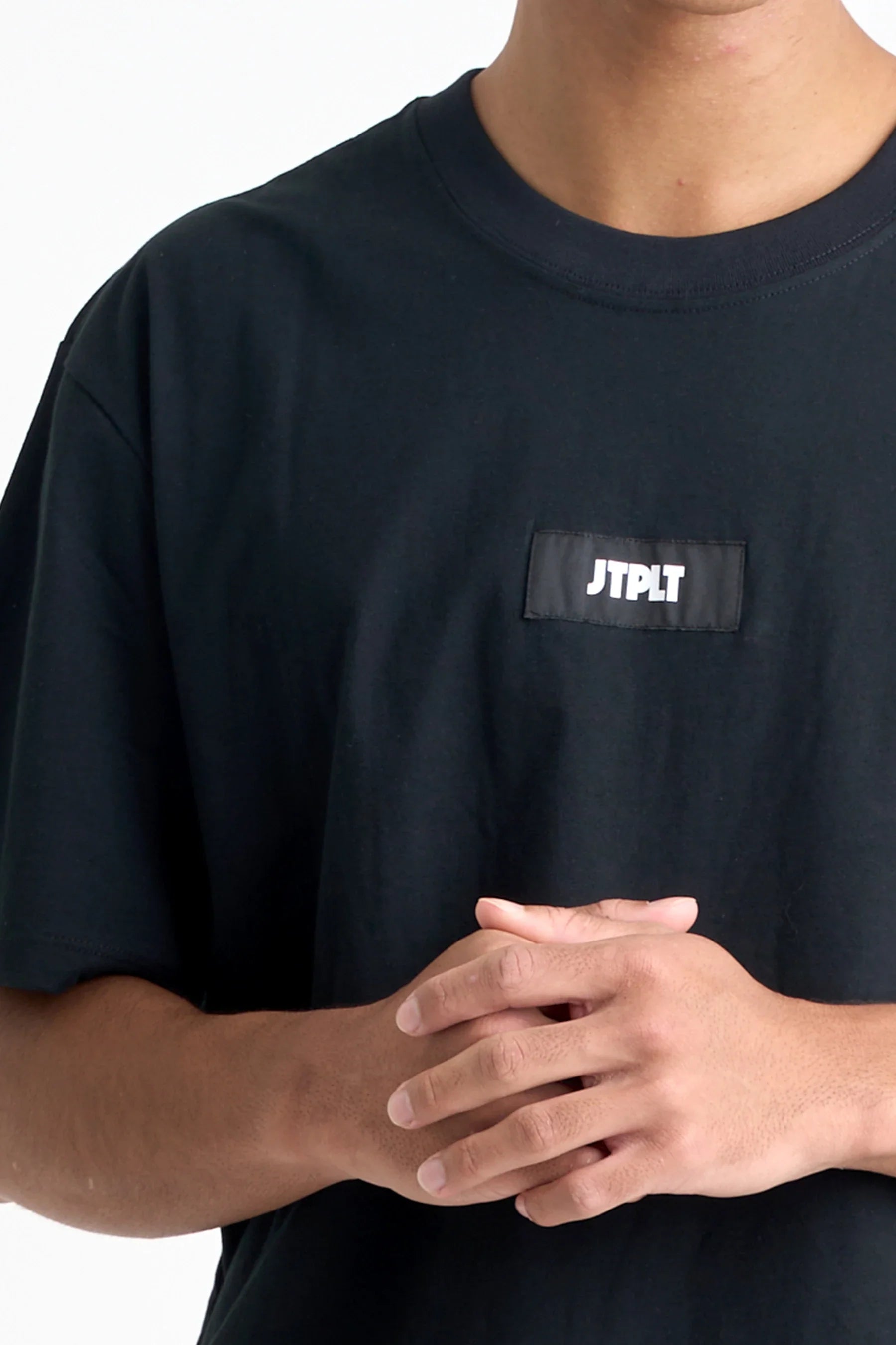 Person wearing a Jetpilot Staple Tee - Black t-shirt with a logo 'JTPLT' patch on a white background