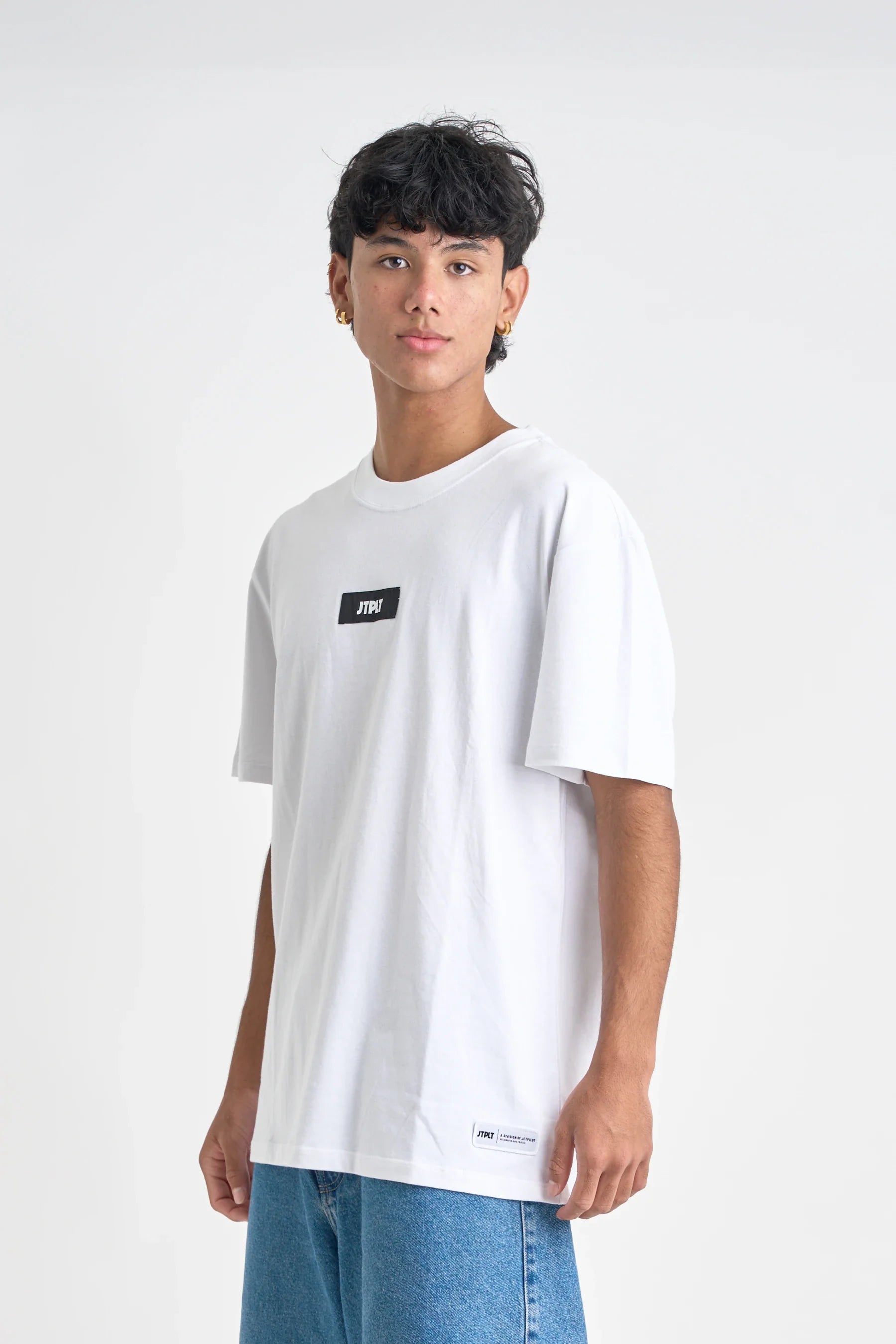 Person wearing a white t-shirt with a small black logo on a plain background