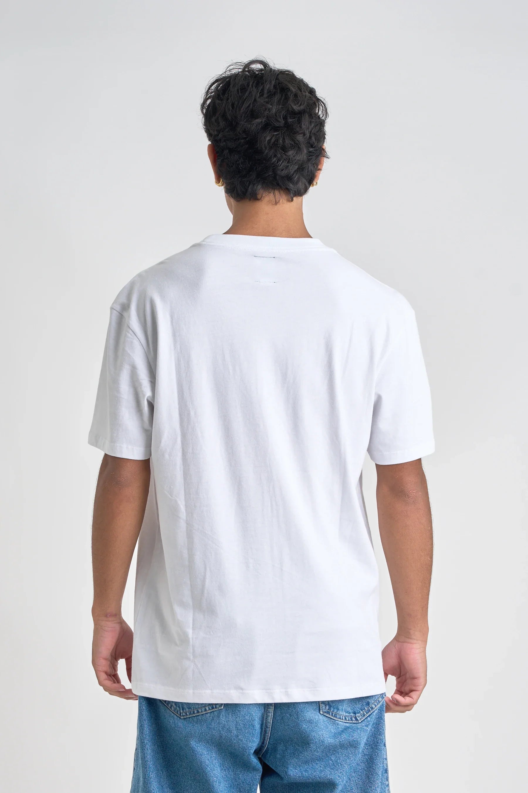 Person wearing a Jetpilot Staple Tee - White t-shirt and blue jeans on a light gray background