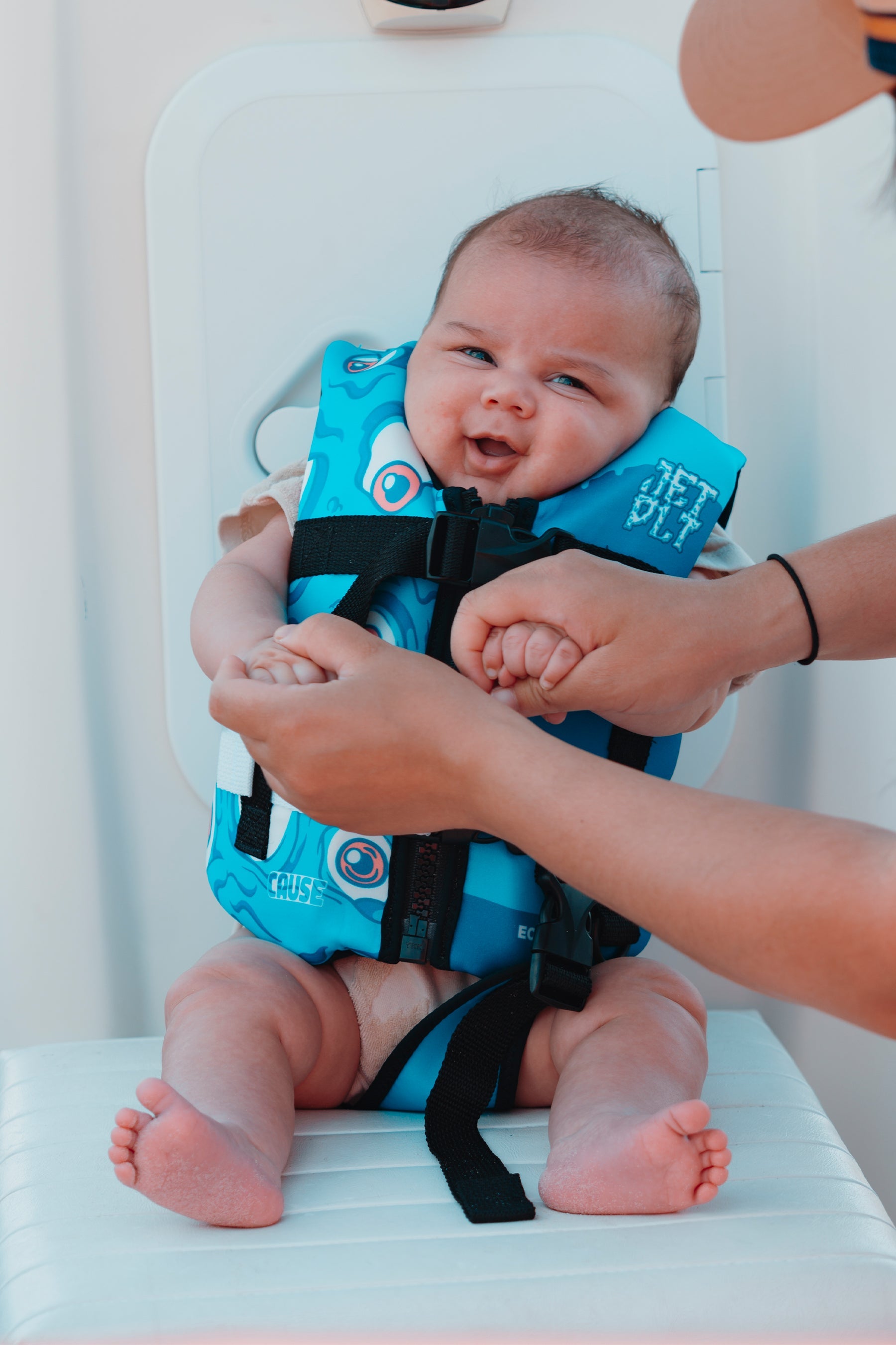 Baby wearing a blue life jacket with an adult adjusting it, on a white background