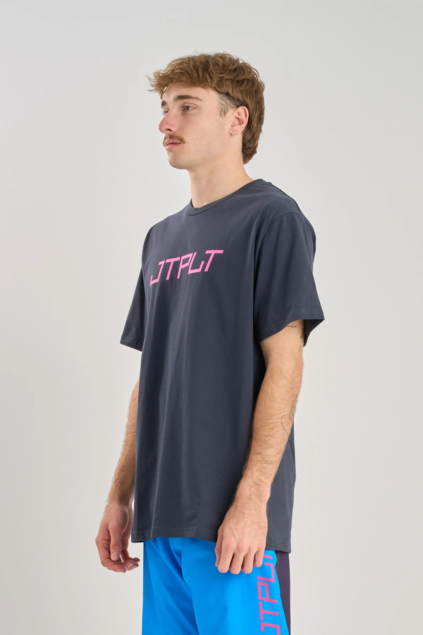 Person wearing a Jetpilot Vault SS Tee - Navy with pink text on a light gray background