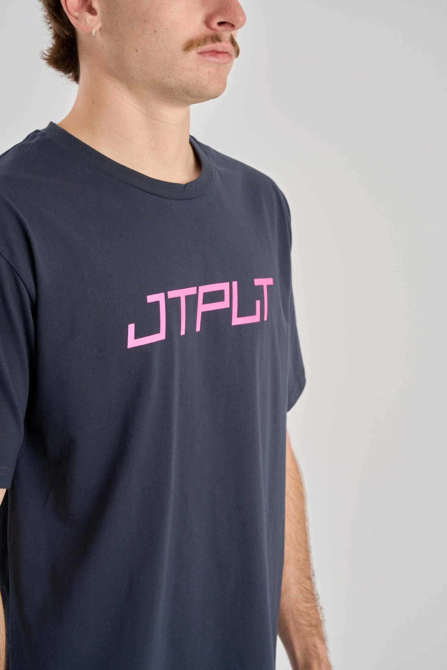 Person wearing a navy t-shirt with pink logo on a plain background